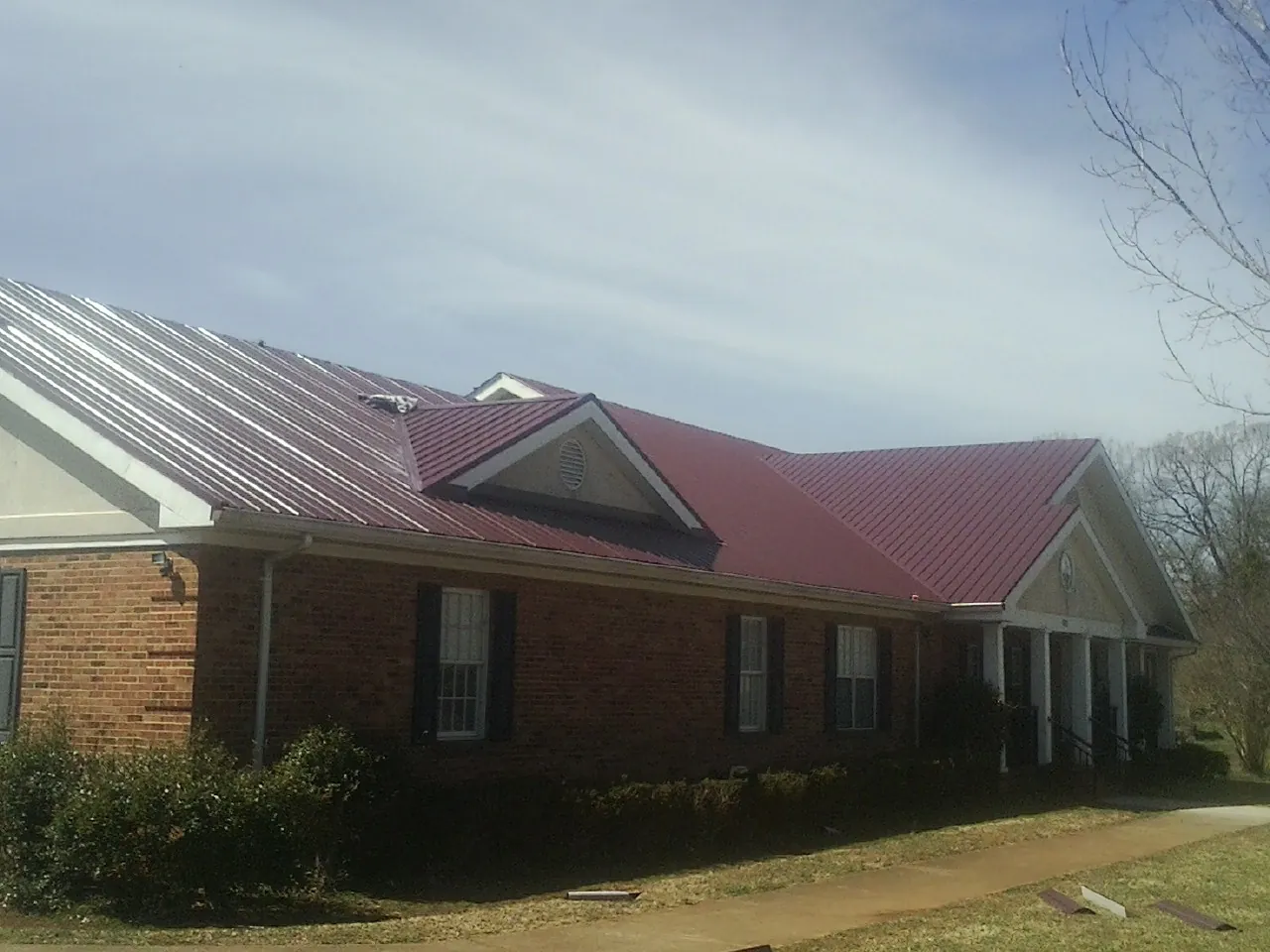 Red metal roof with gabled entries on a long brick building, from a Hail Damage Roof Repair job in Sioux City