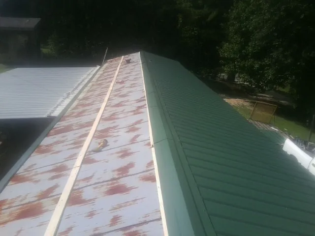 Old rusted panels beside newly installed green metal roofing — Wind Damage Roof Repair by Roofing Brothers in Sioux City