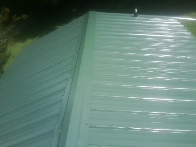 New green metal panels meeting at the ridge of a roof — Flat Roof Repair work by our crew in Sioux City