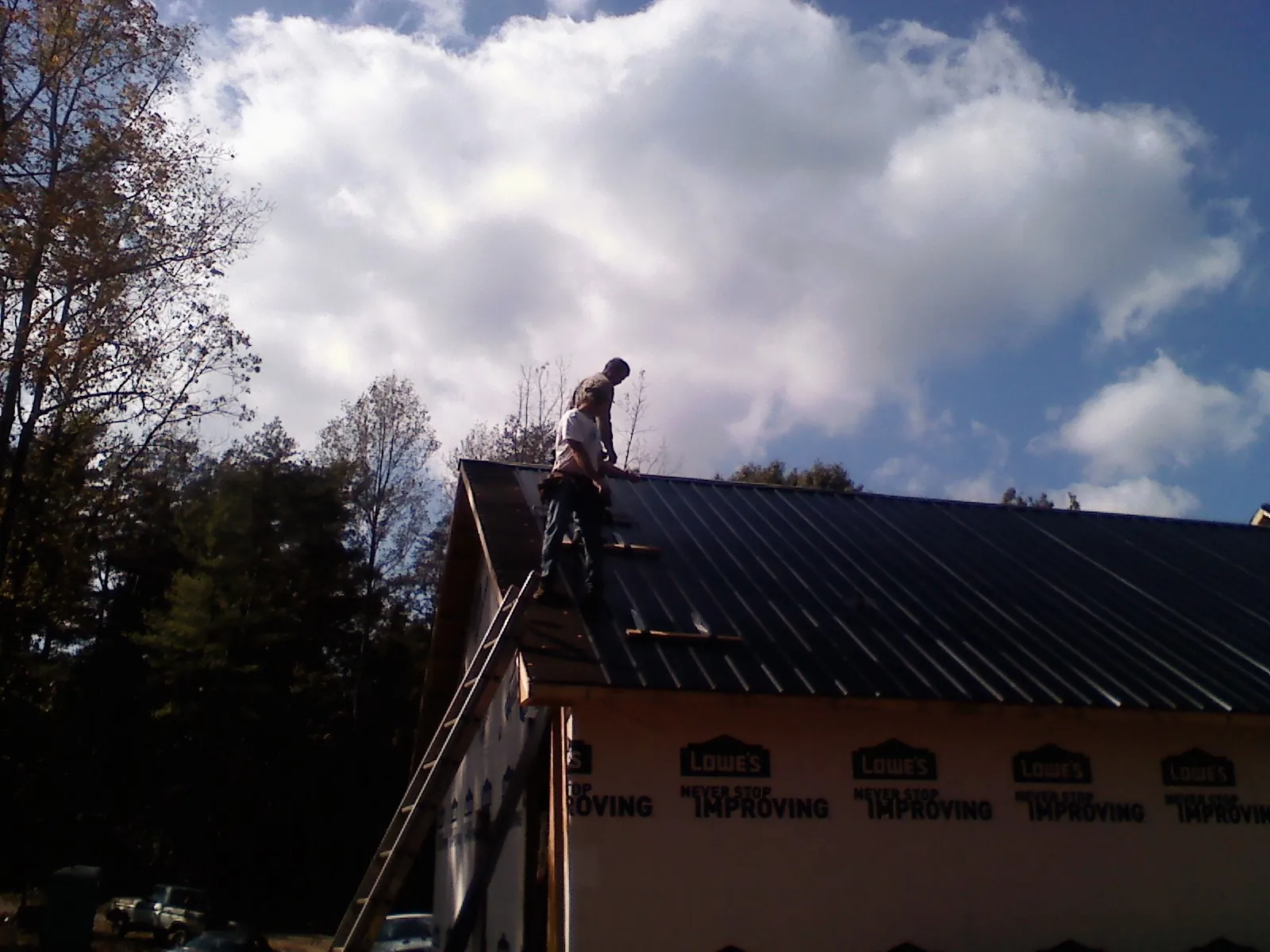 Roofer fastening dark metal panels high against a cloudy sky, from a Roof Inspection job in Sioux City