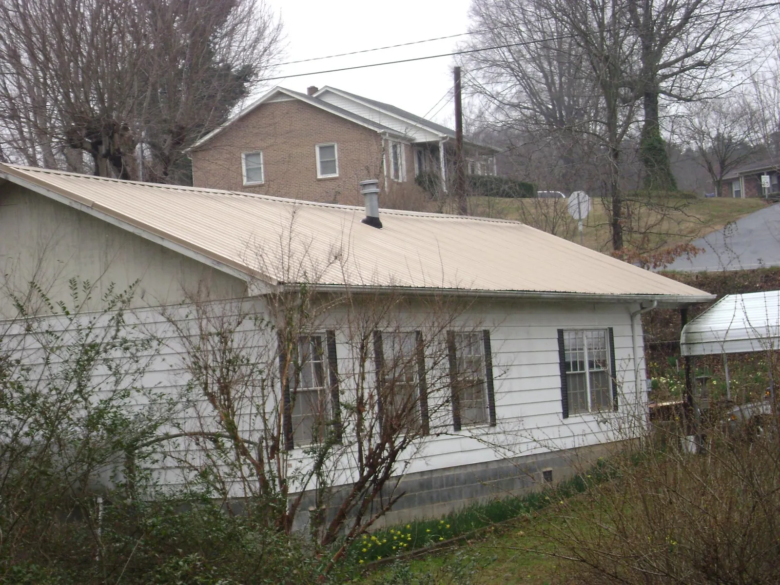 Tan metal roof on a white sided house set into a hillside — Commercial Roofing by Roofing Brothers in Sioux City